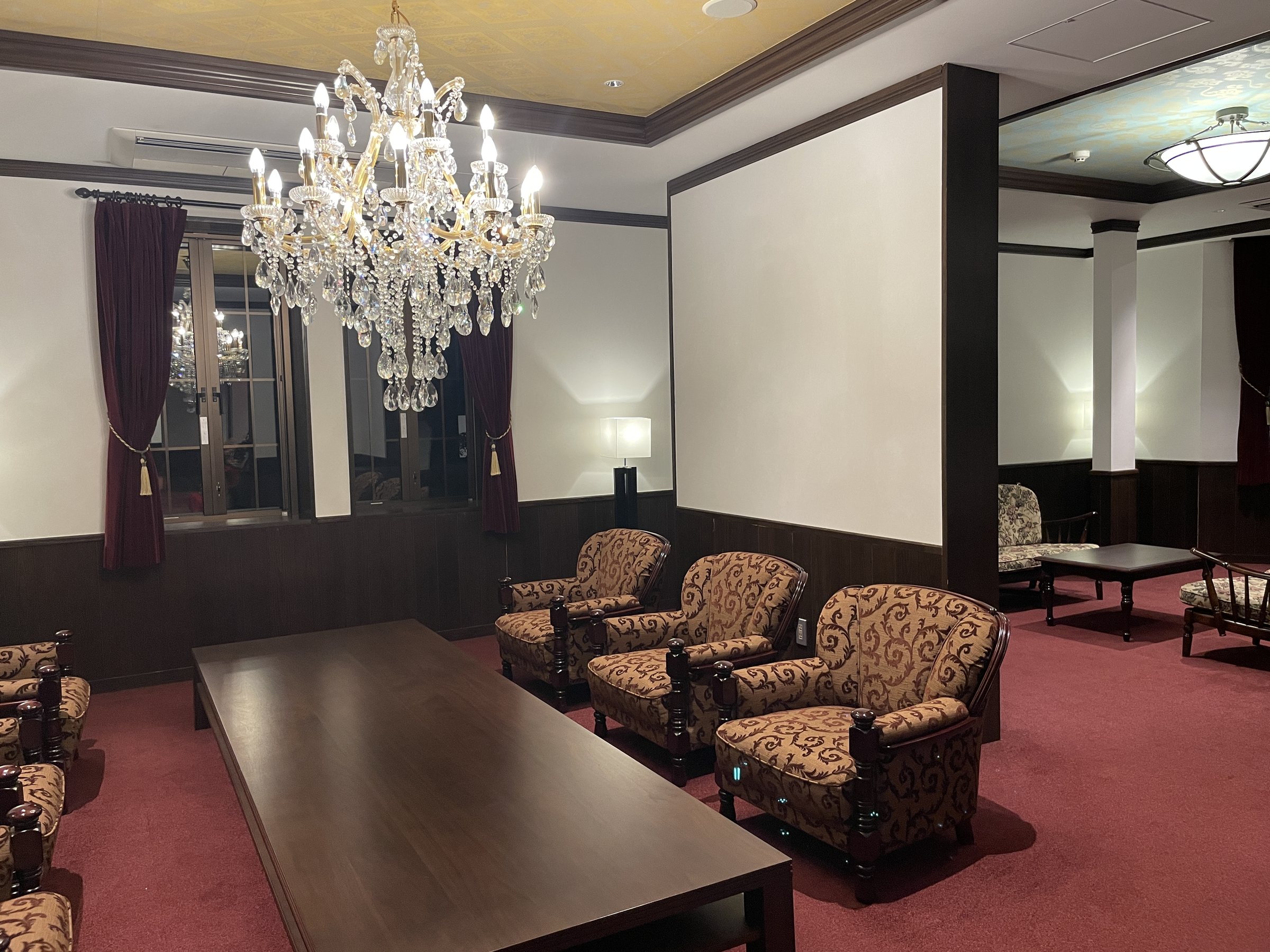 The lounge beneath a crystal chandelier: patterned armchairs on a deep red carpet.