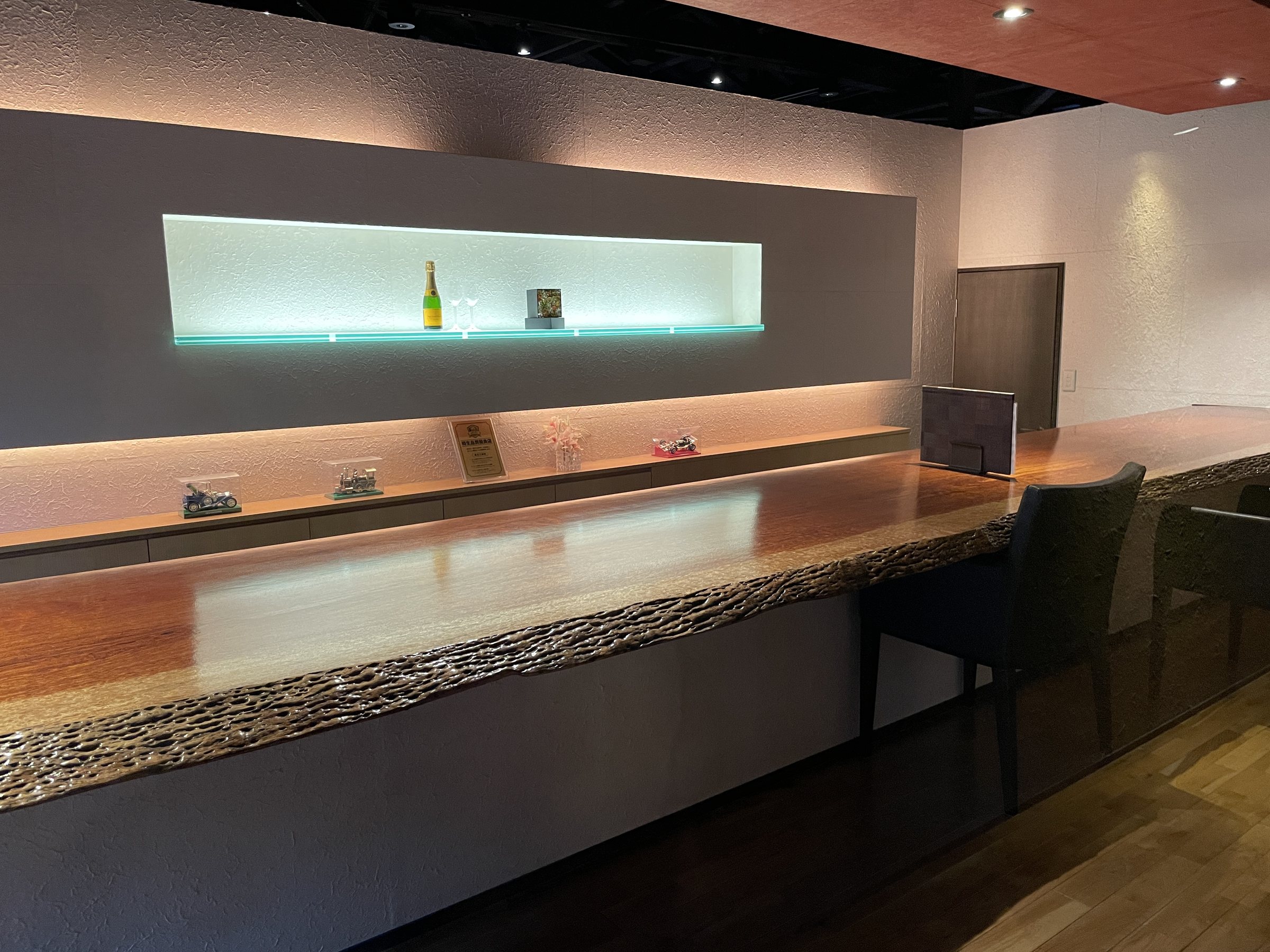 The bar: a long wooden counter beneath a backlit shelf.