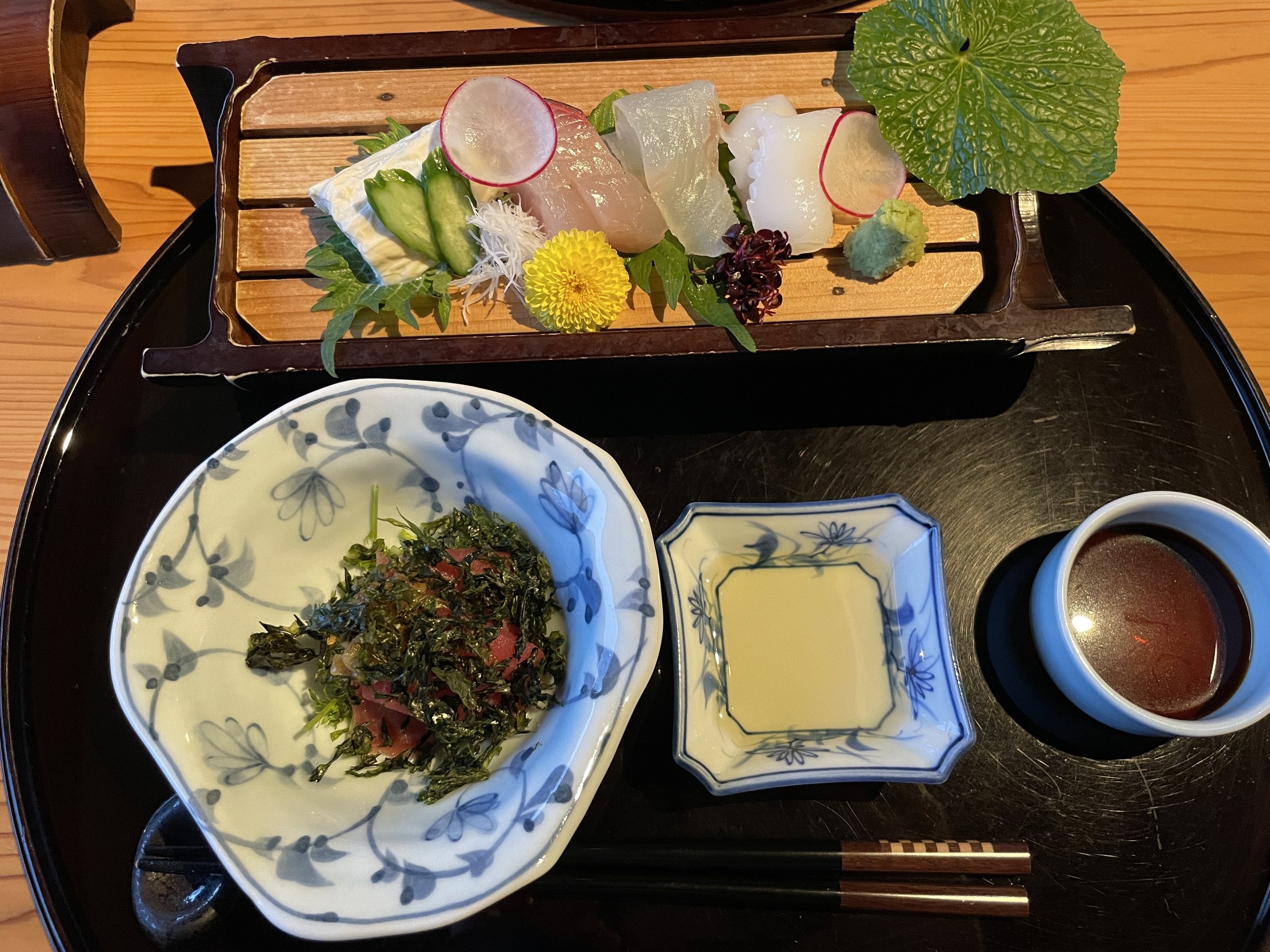 Sashimi on a long wooden board, with a bowl of dressed tuna and seaweed and a dish of soy sauce.