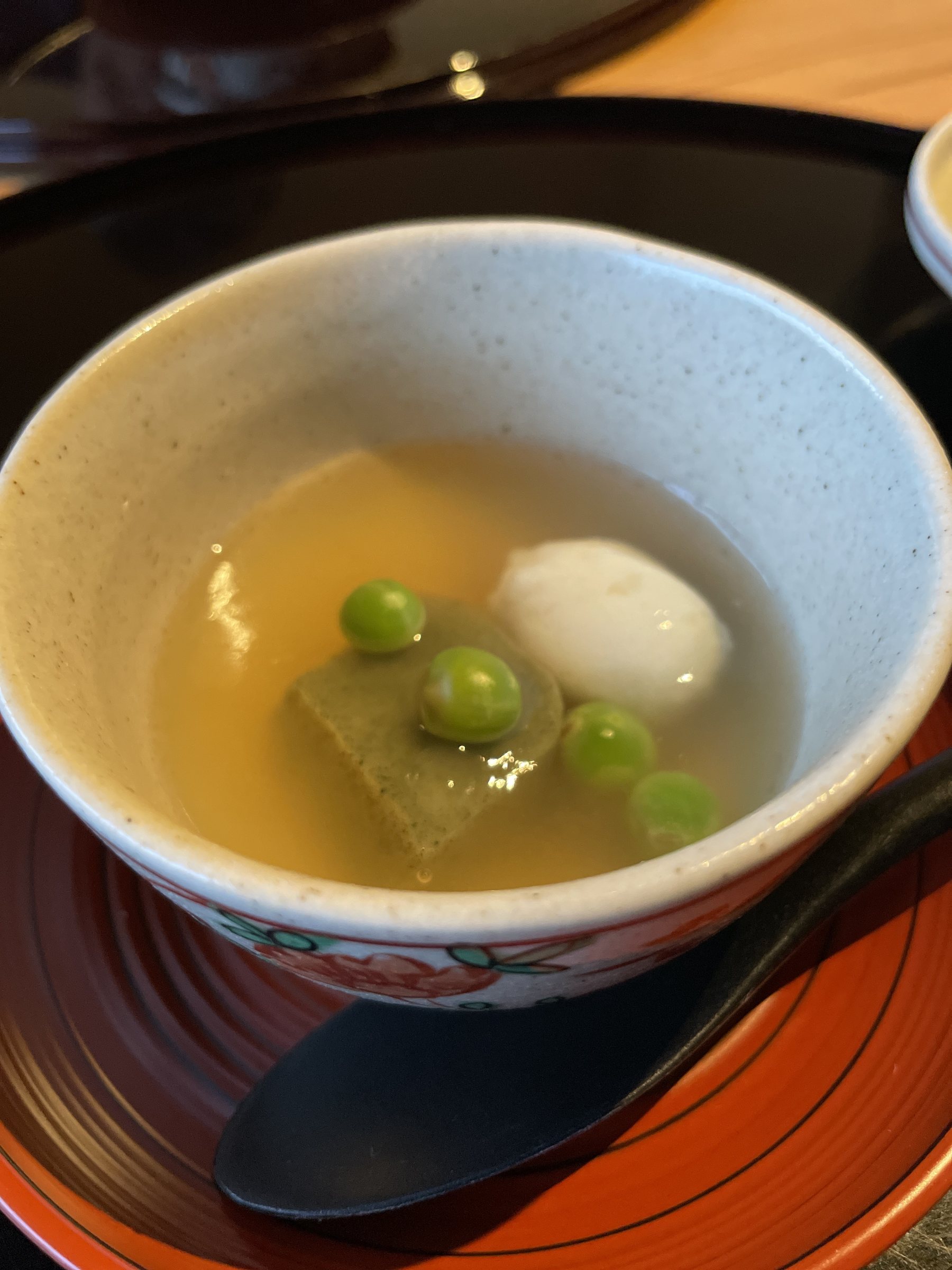 A round white dumpling and green peas in a clear broth.