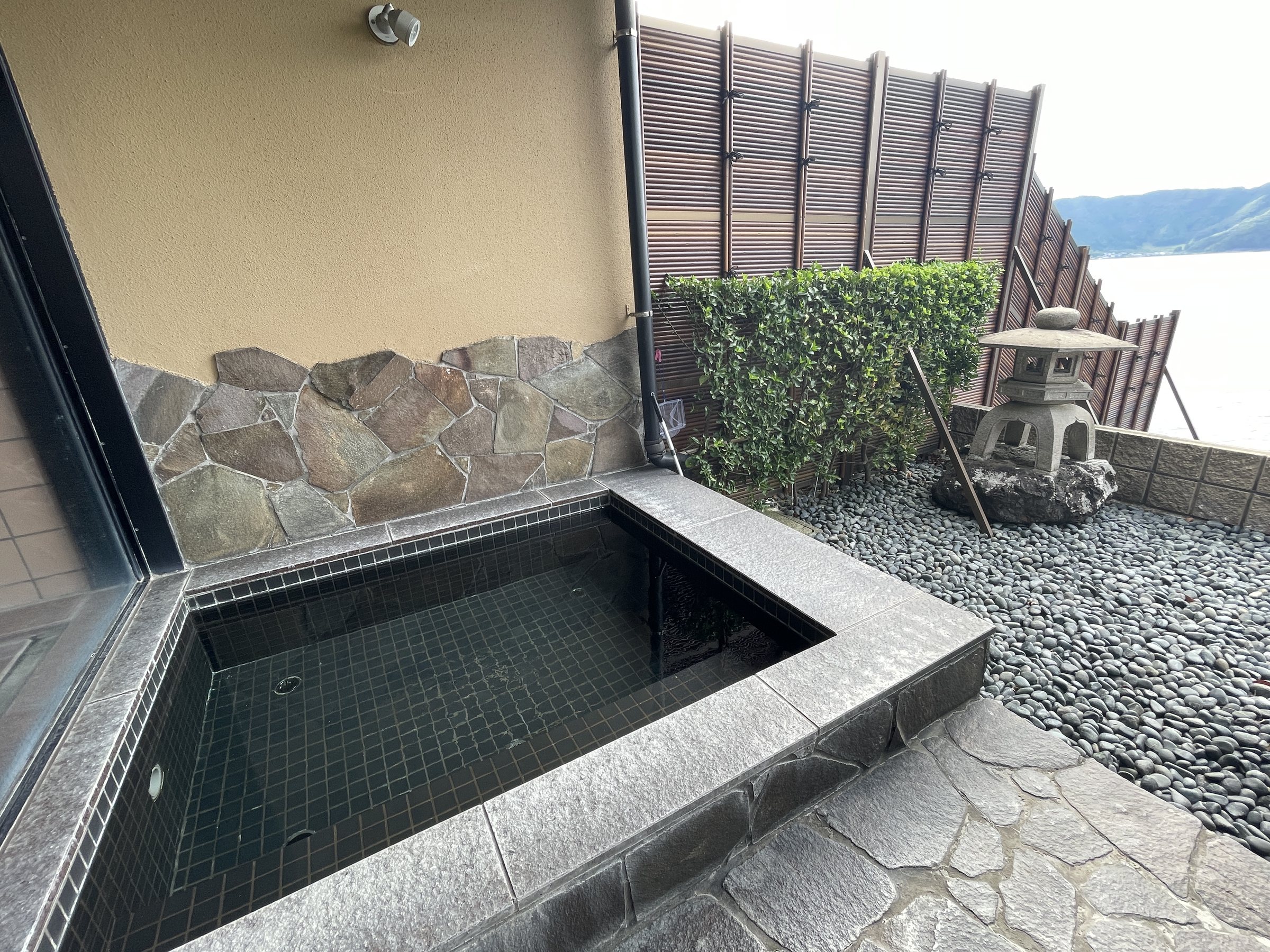 The small open-air bath, edged with stone, beside a garden lantern.