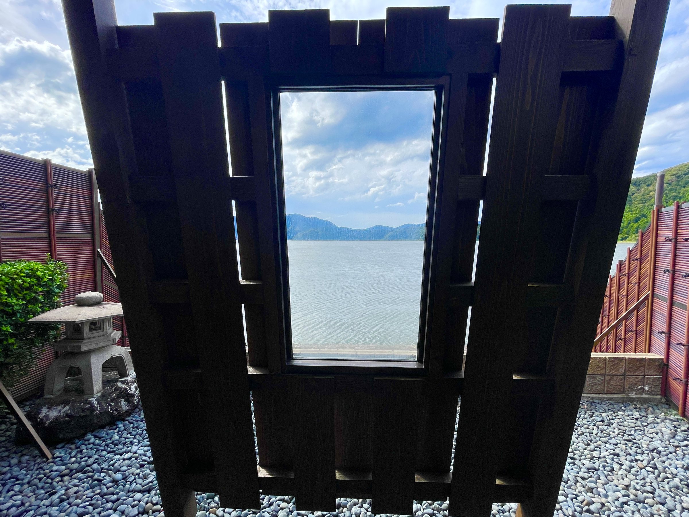 A wooden screen with a window-like opening, framing the lake from the open-air bath.