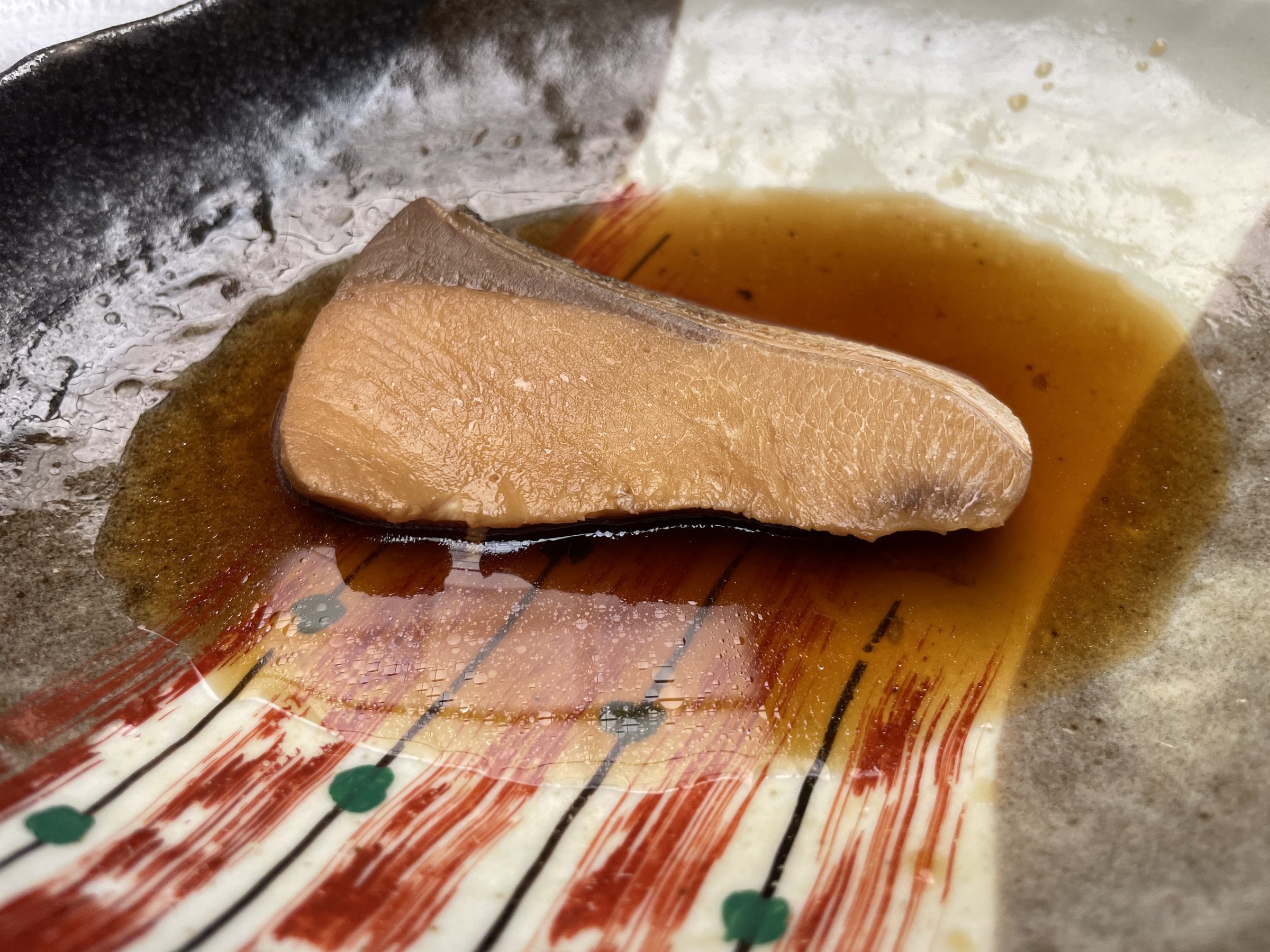 A fillet of yellowtail in a glossy dark sauce on a decorated plate.