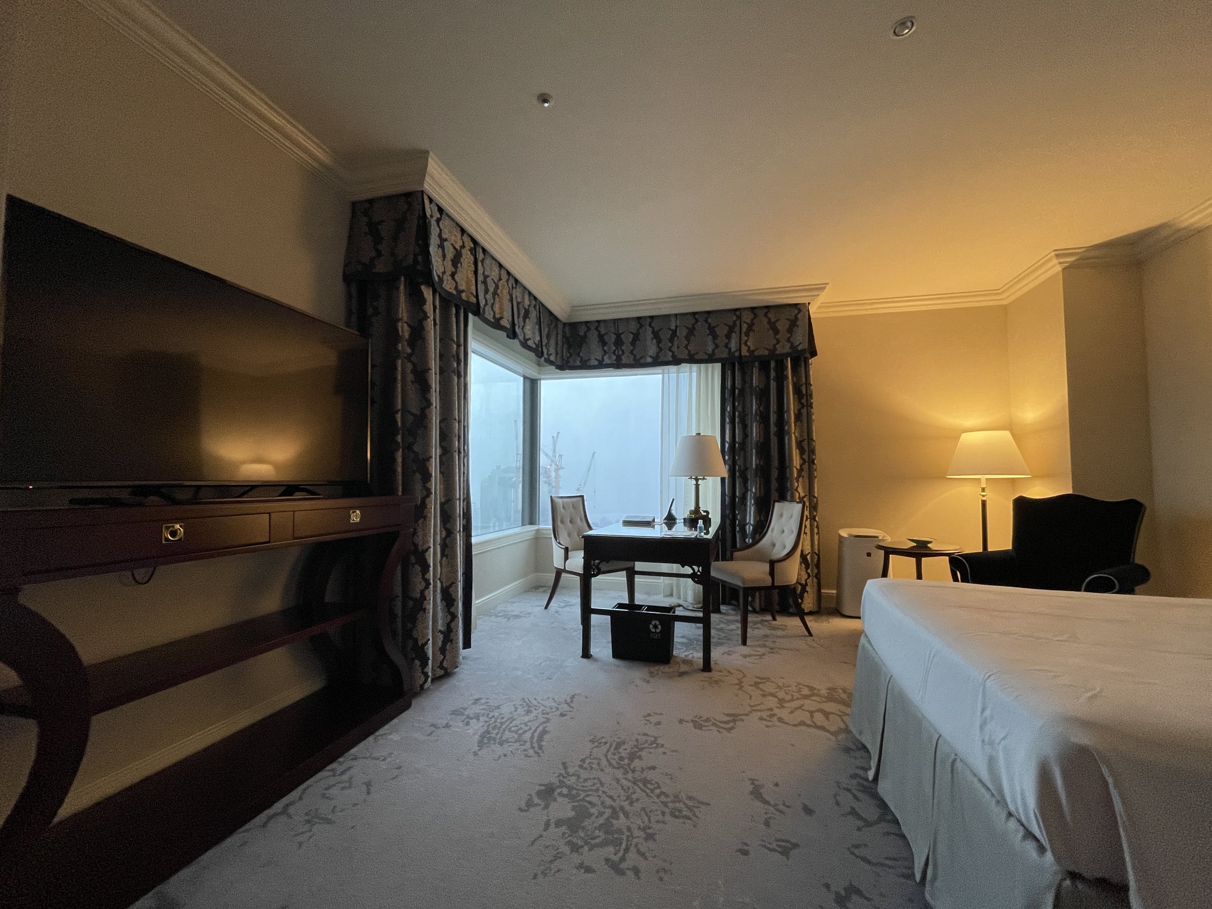 The room from the entrance: a corner window with heavy drapes, a desk and an armchair.