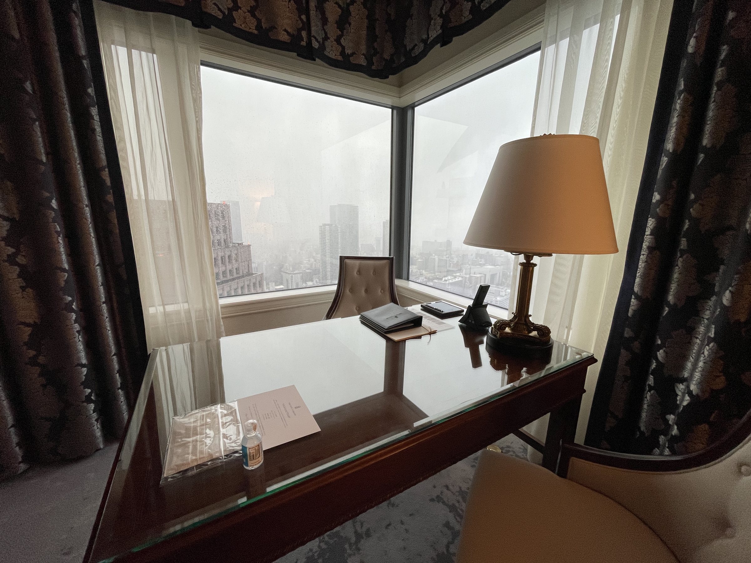 The writing desk in the corner window, with a brass lamp.