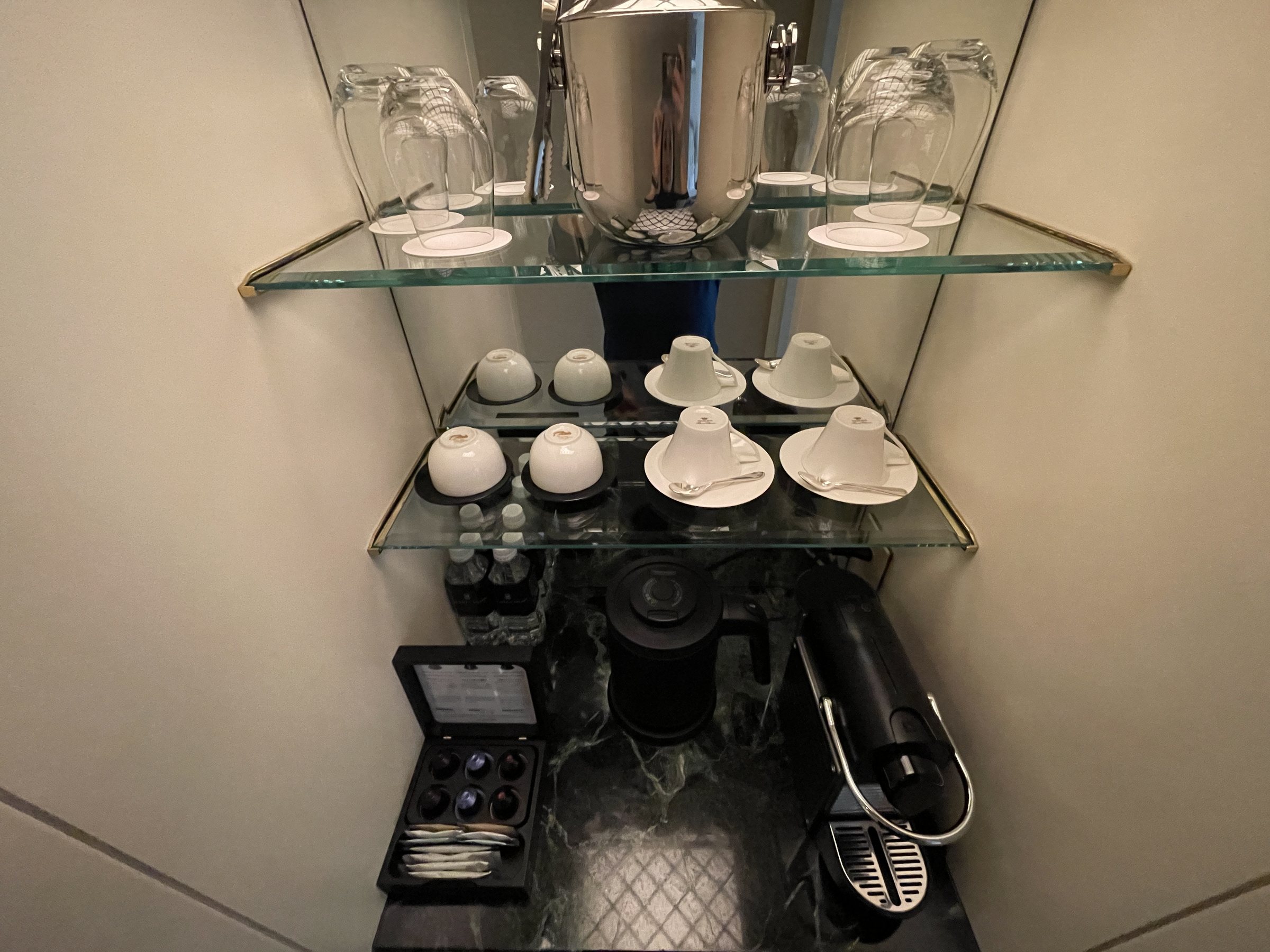 Glass shelves of cups, glasses and an ice bucket, with a coffee machine below.