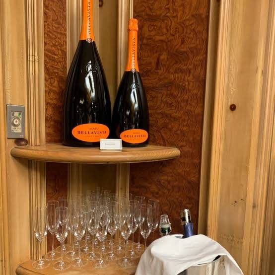Bottles of sparkling wine and glasses set out on a wooden shelf at breakfast.