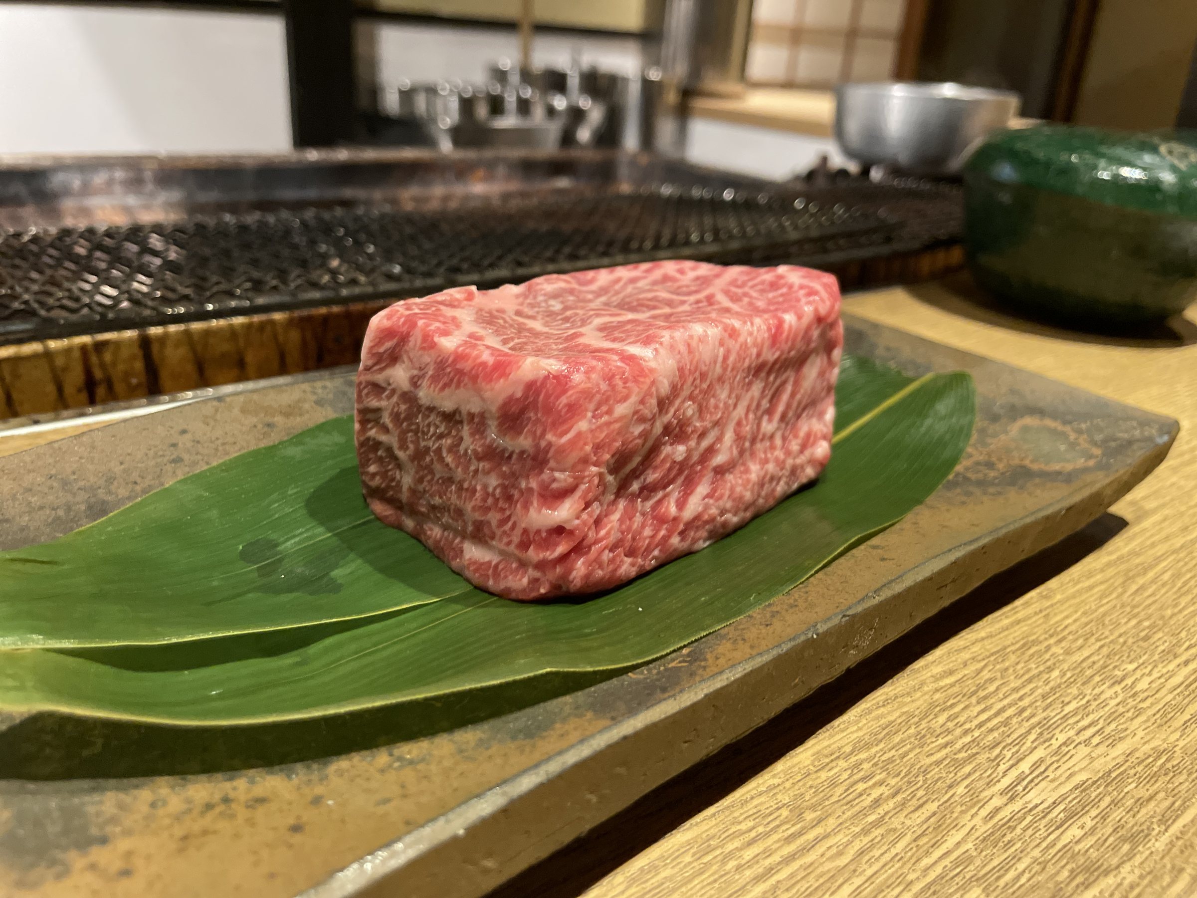 A block of marbled beef on a leaf, waiting beside the grill.