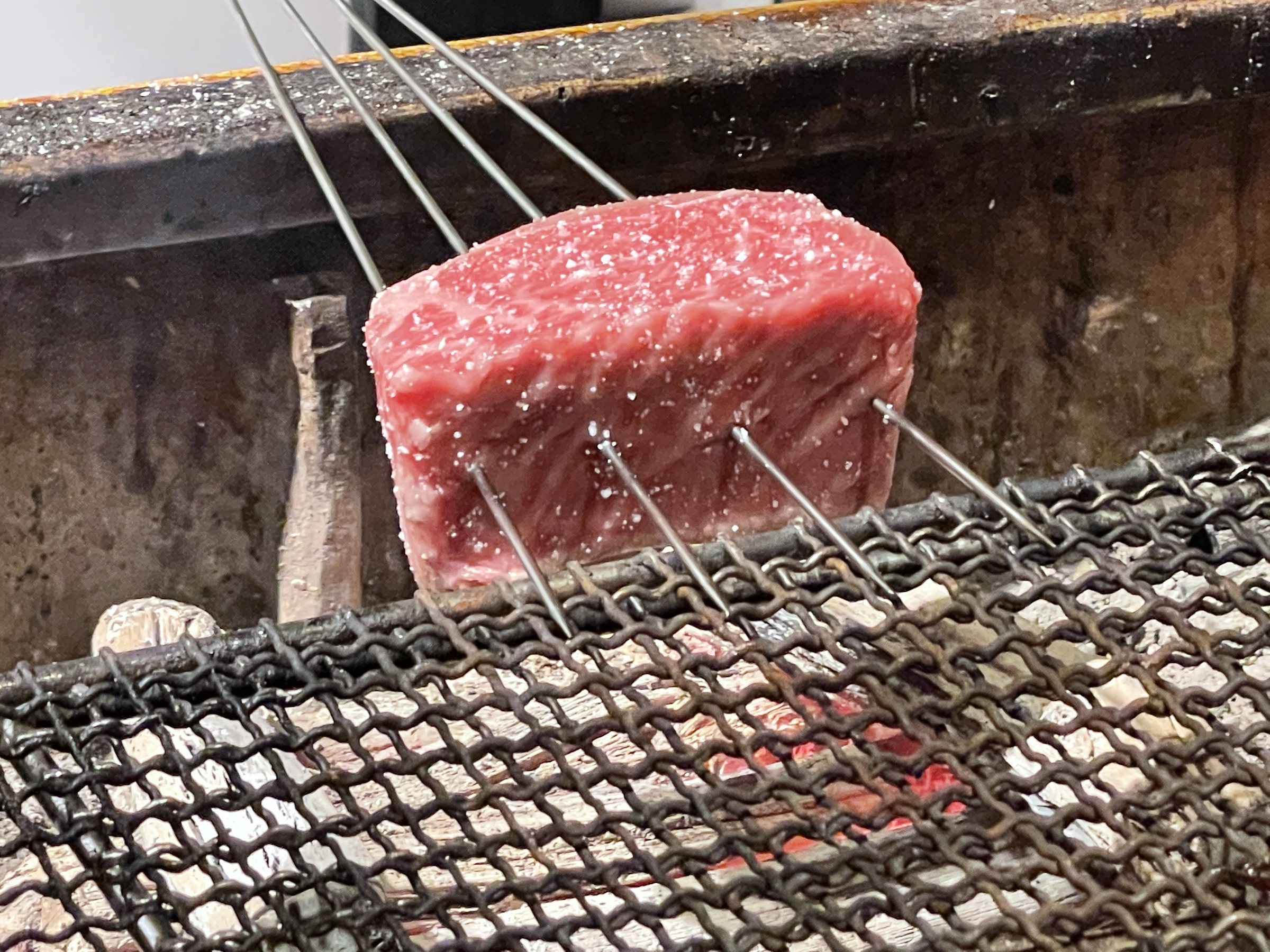 The beef, skewered, begins to roast over glowing charcoal.