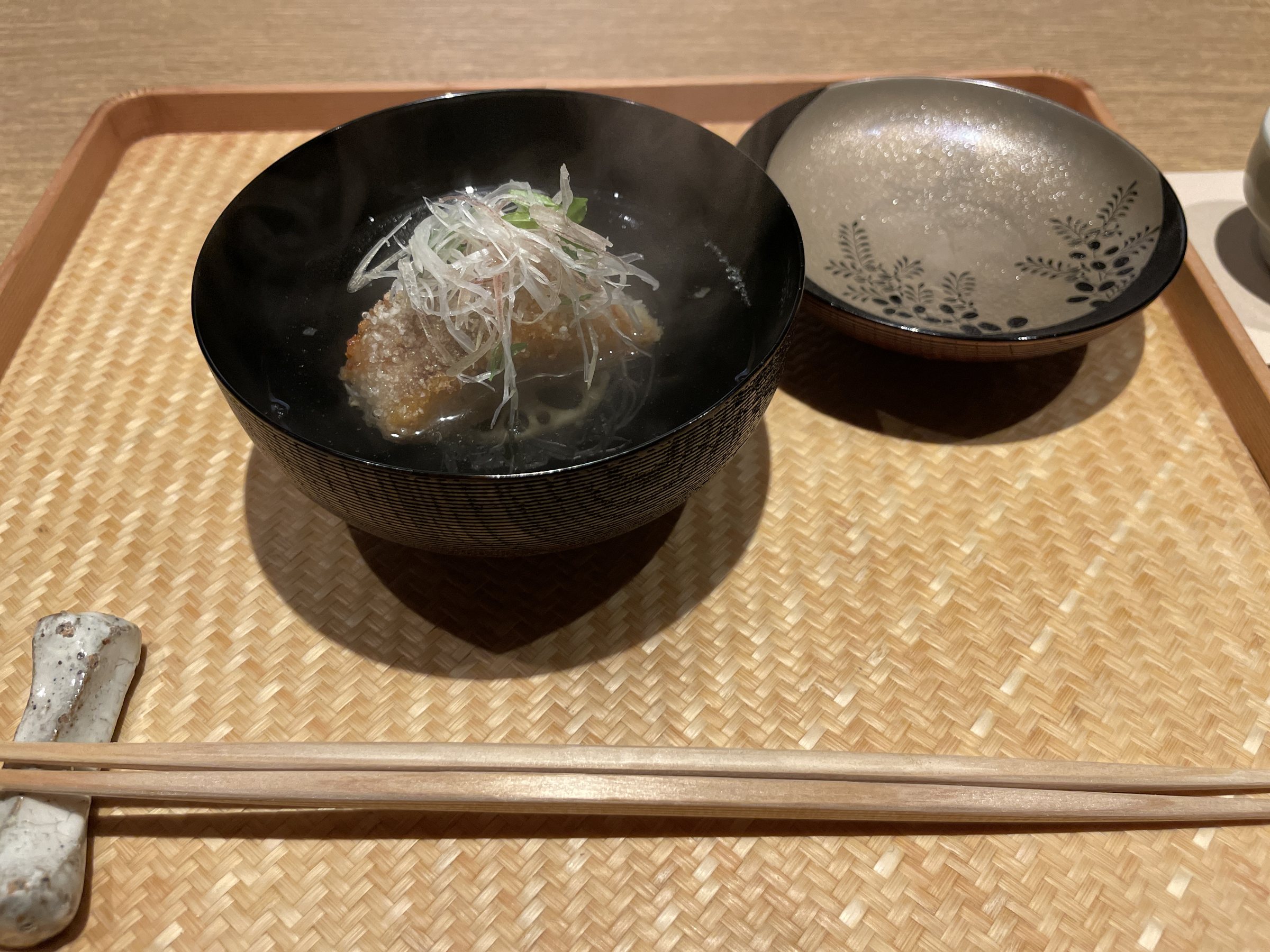 A black lacquered bowl of clear soup with fried fish and fine shreds of vegetable.