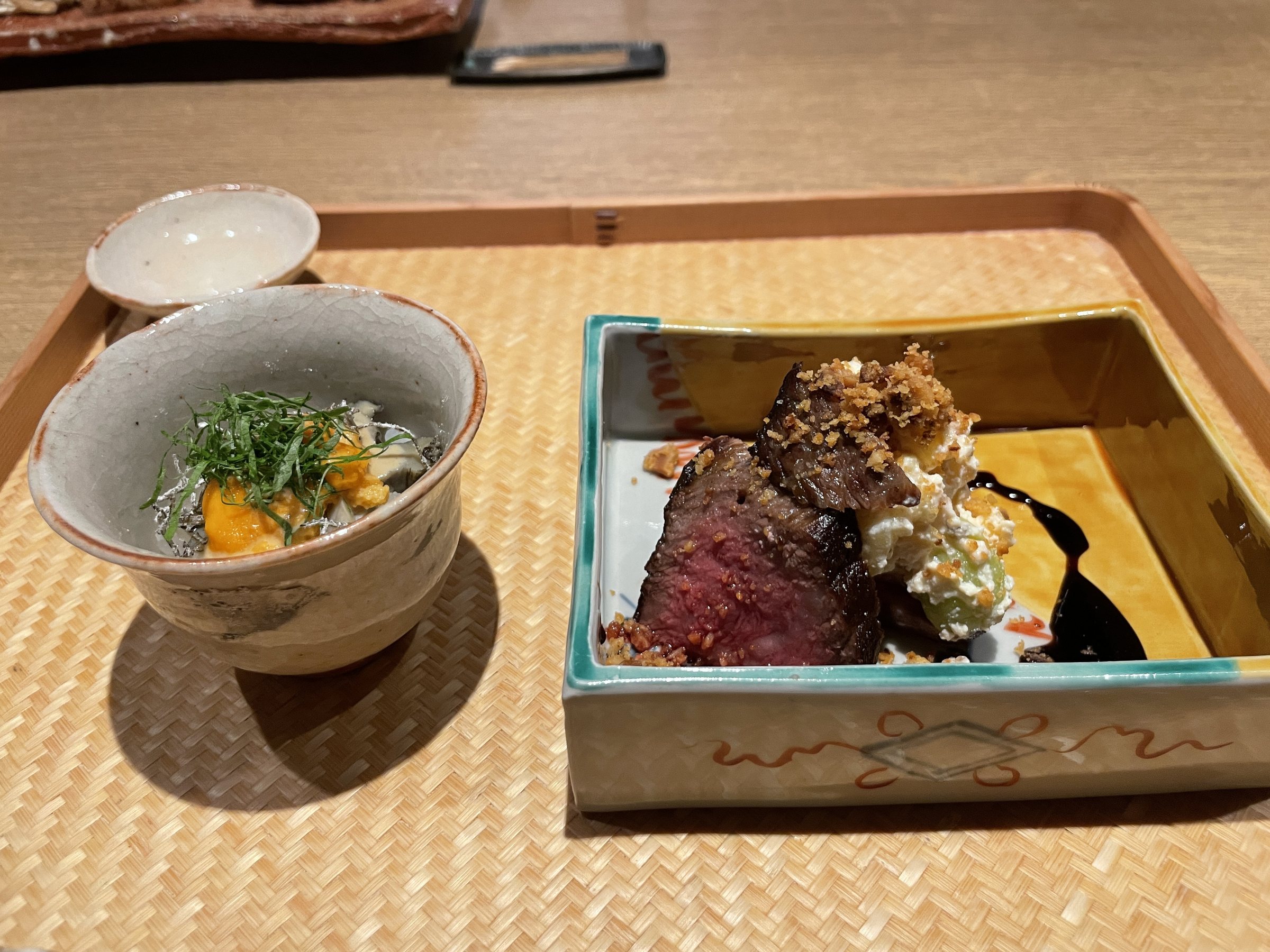 Charcoal-roasted beef in a square dish beside a small bowl of sea urchin and abalone.