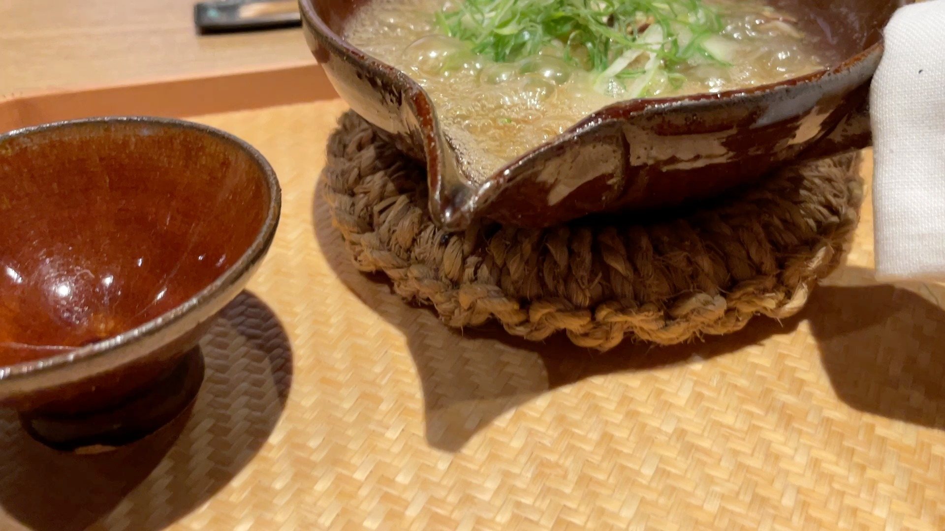 A bubbling earthenware dish of thick broth topped with green leek.