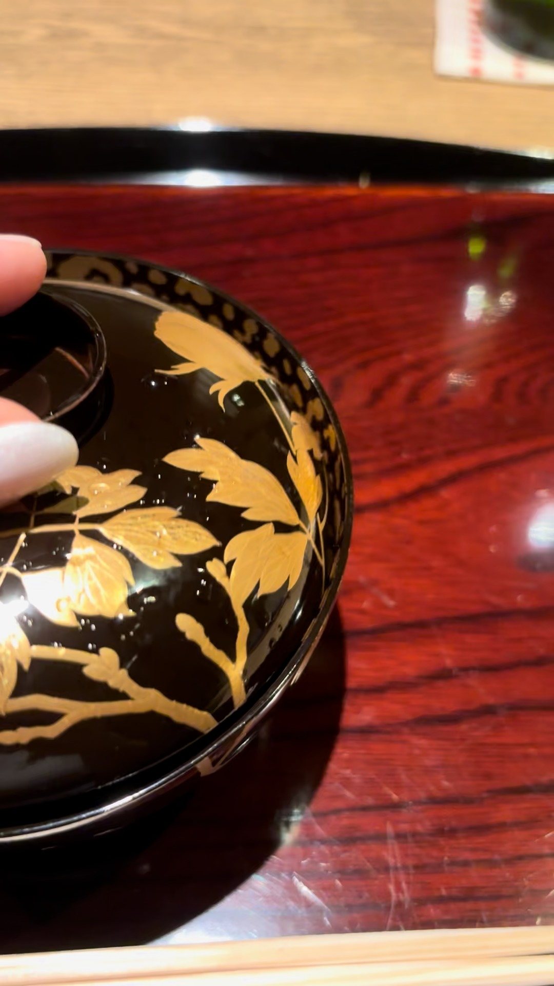 The lid of a black and gold lacquered soup bowl.