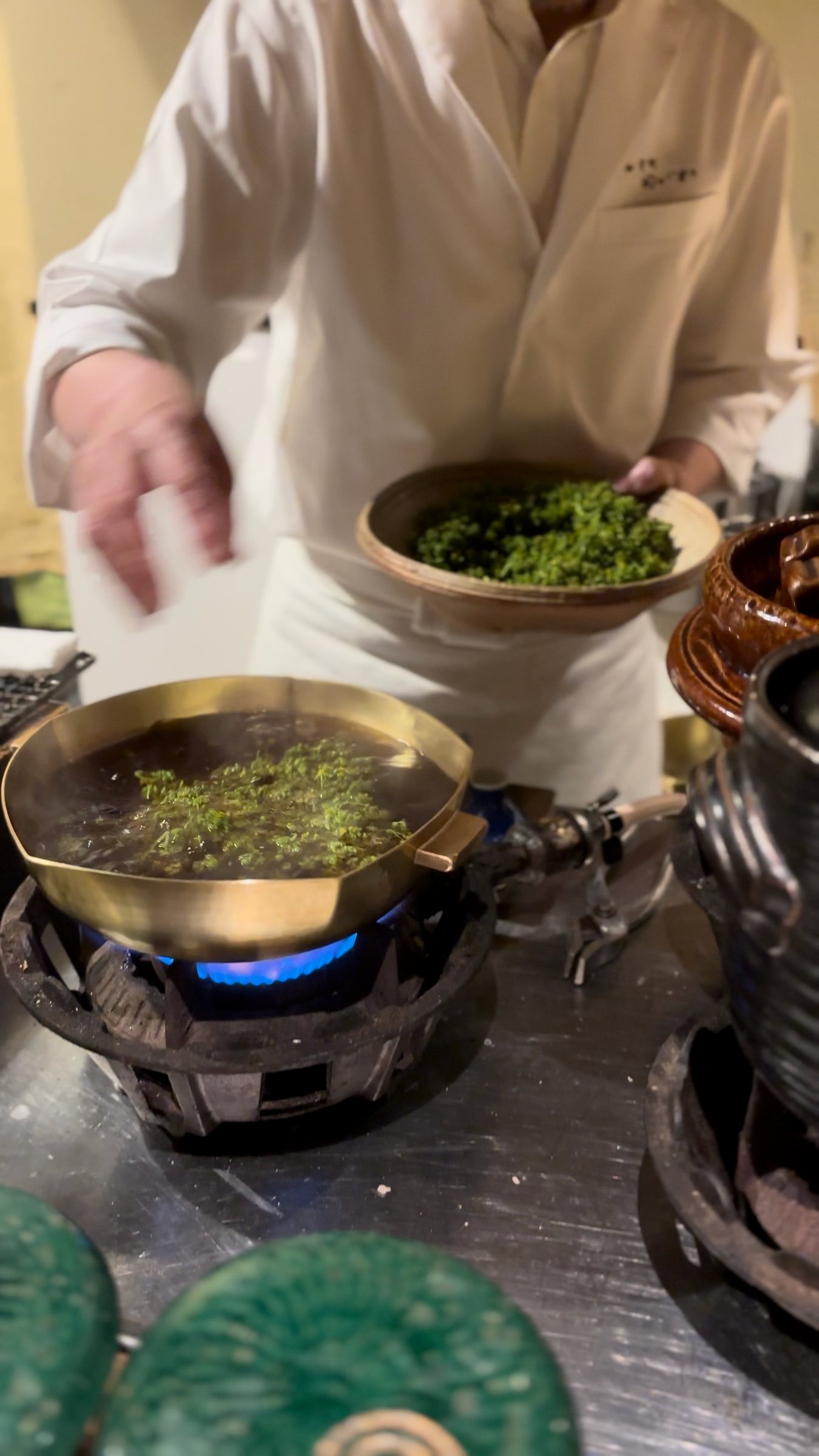 Flower sansho being dipped into hot broth in a brass pan.