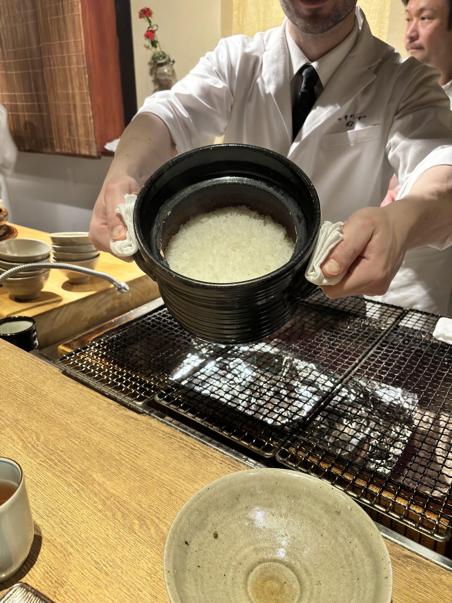 A cook presents an earthenware pot of plain white rice.
