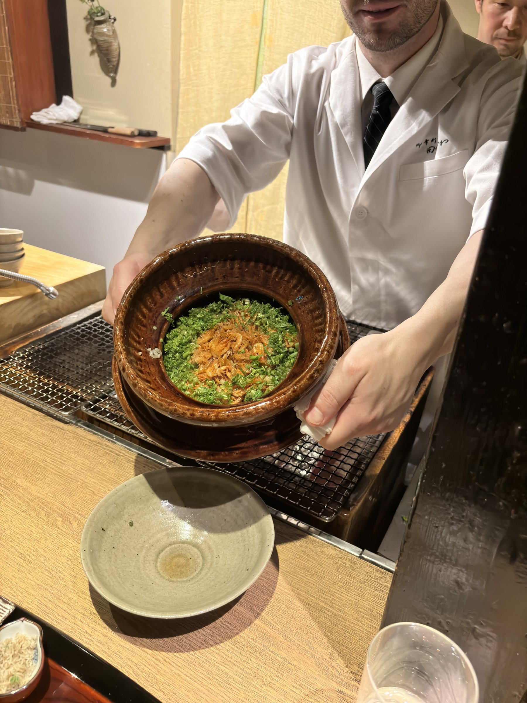 A pot of rice cooked with sakura shrimp and topped with greens.