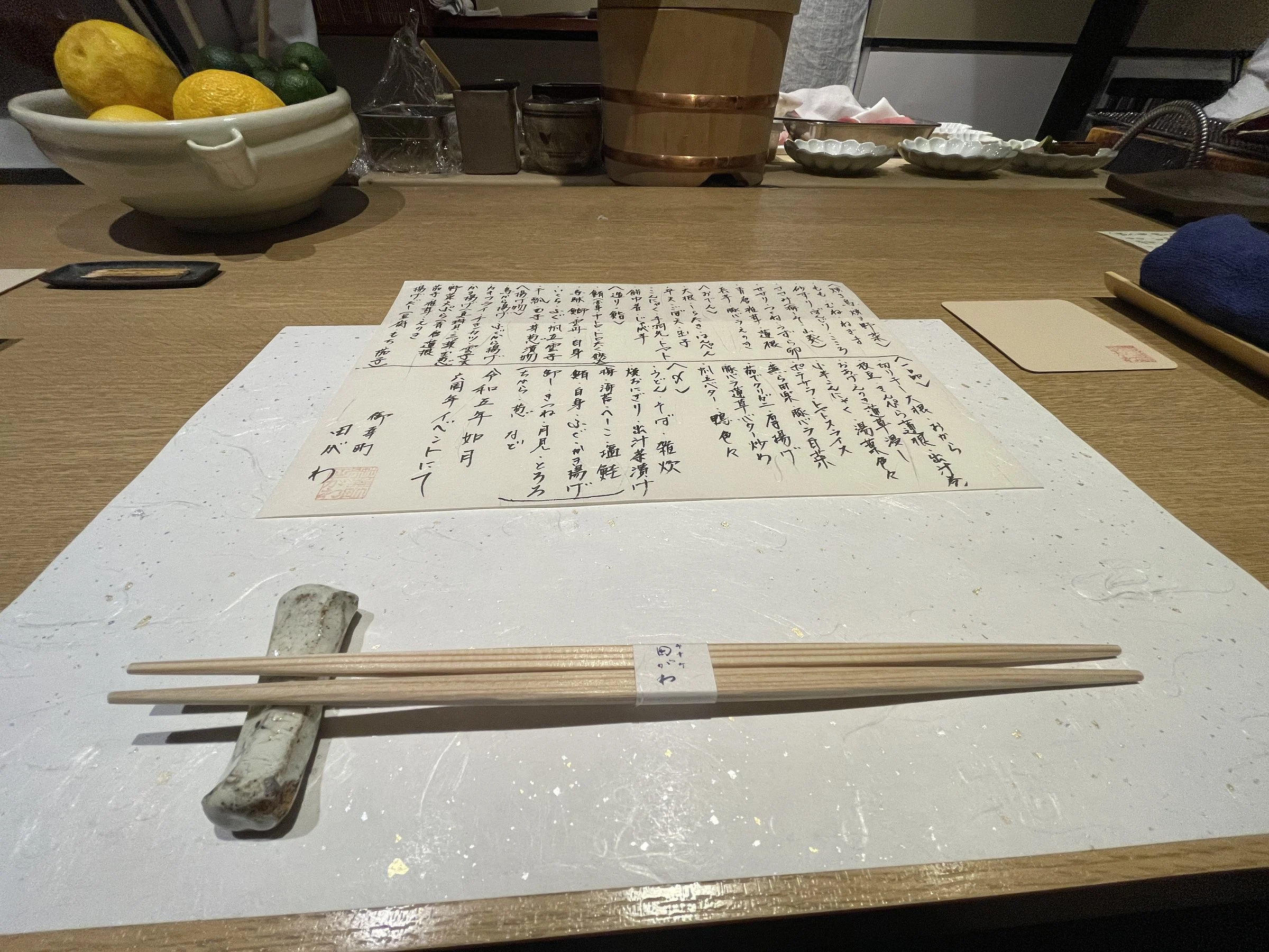 A handwritten menu and chopsticks at the counter, a bowl of citrus beyond.