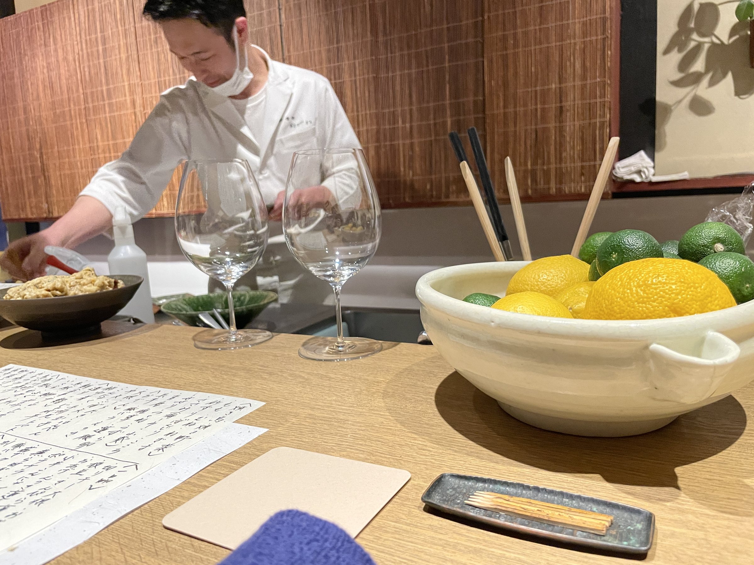 A cook behind the counter, with wine glasses and a bowl of yuzu and sudachi in front.