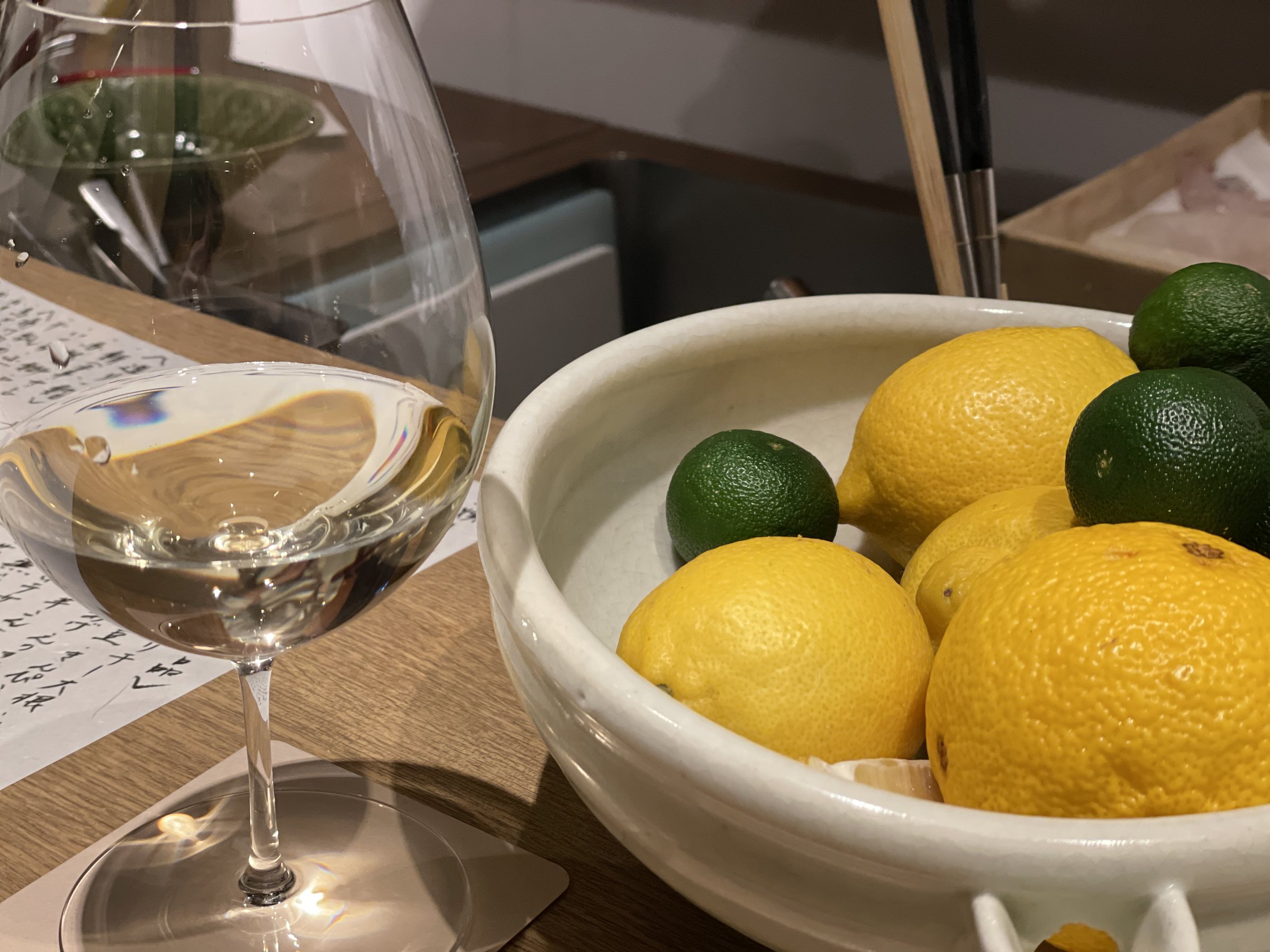 A glass of white wine beside a bowl of citrus.