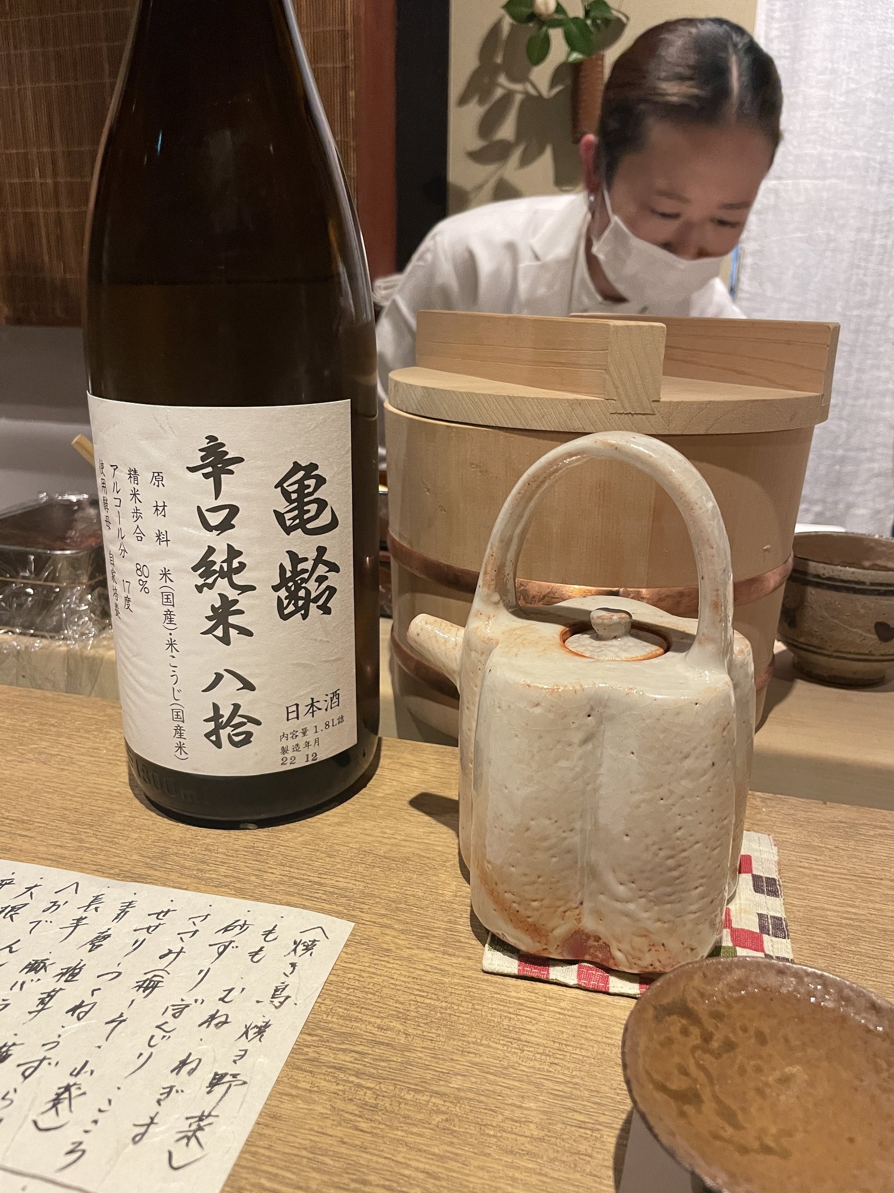 A bottle of Kirei dry junmai sake, with a cook behind the counter.