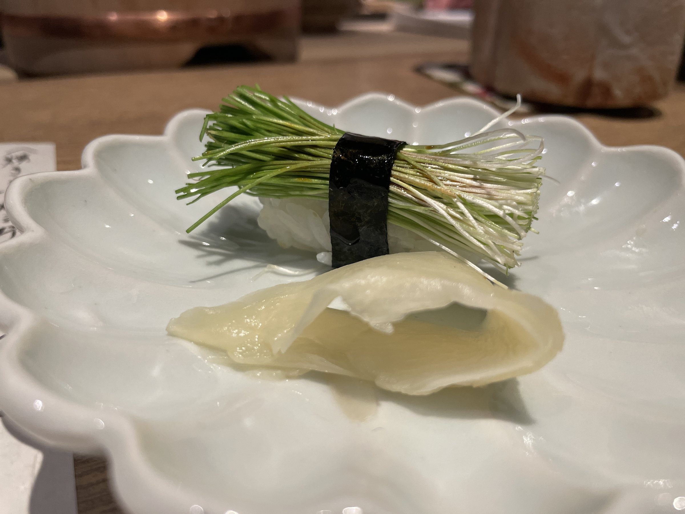 Menegi sushi: a bundle of young leek sprouts tied with a band of nori, with pickled ginger.