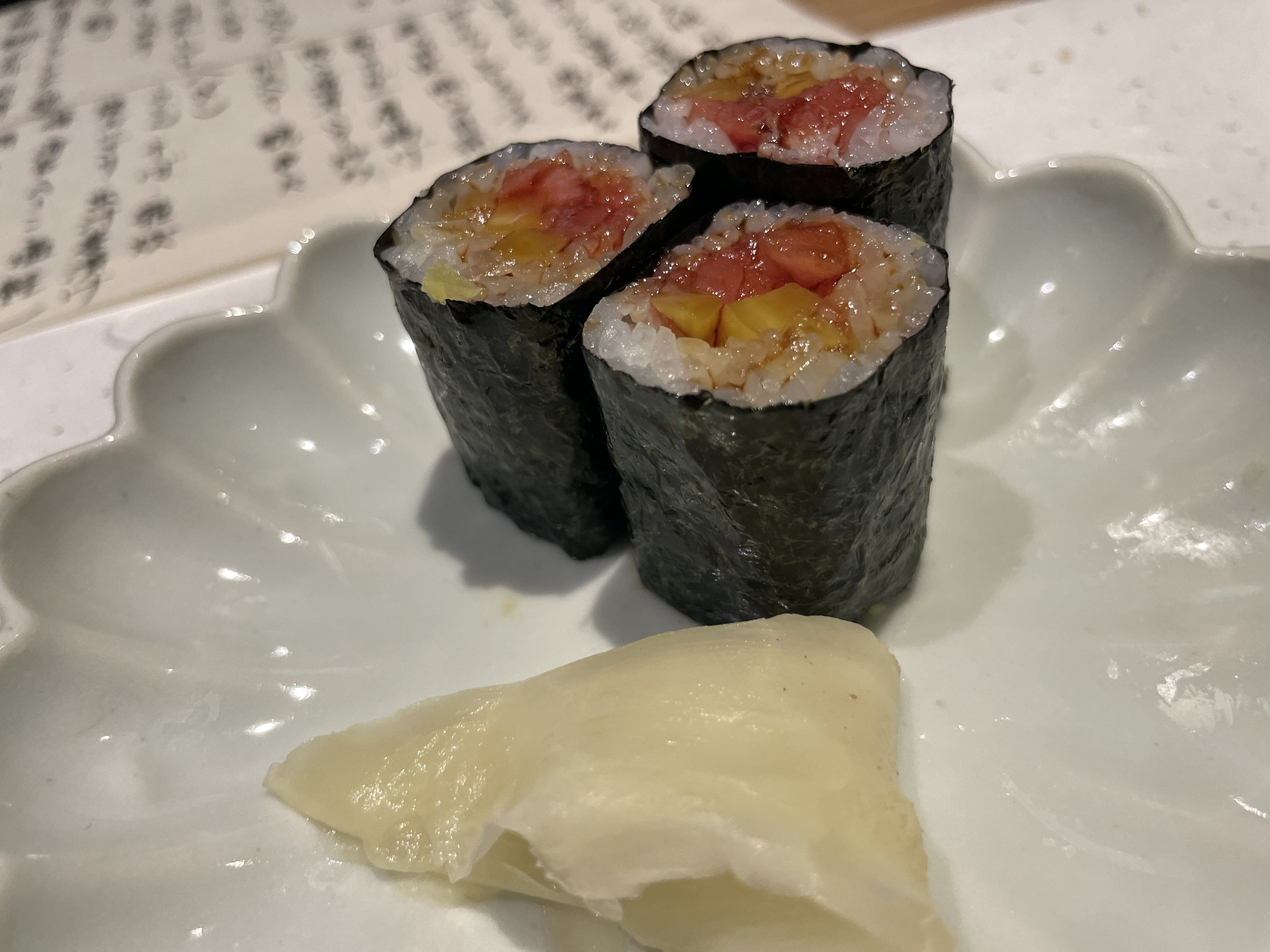 Tuna rolls with pickled ginger on a scalloped white plate.