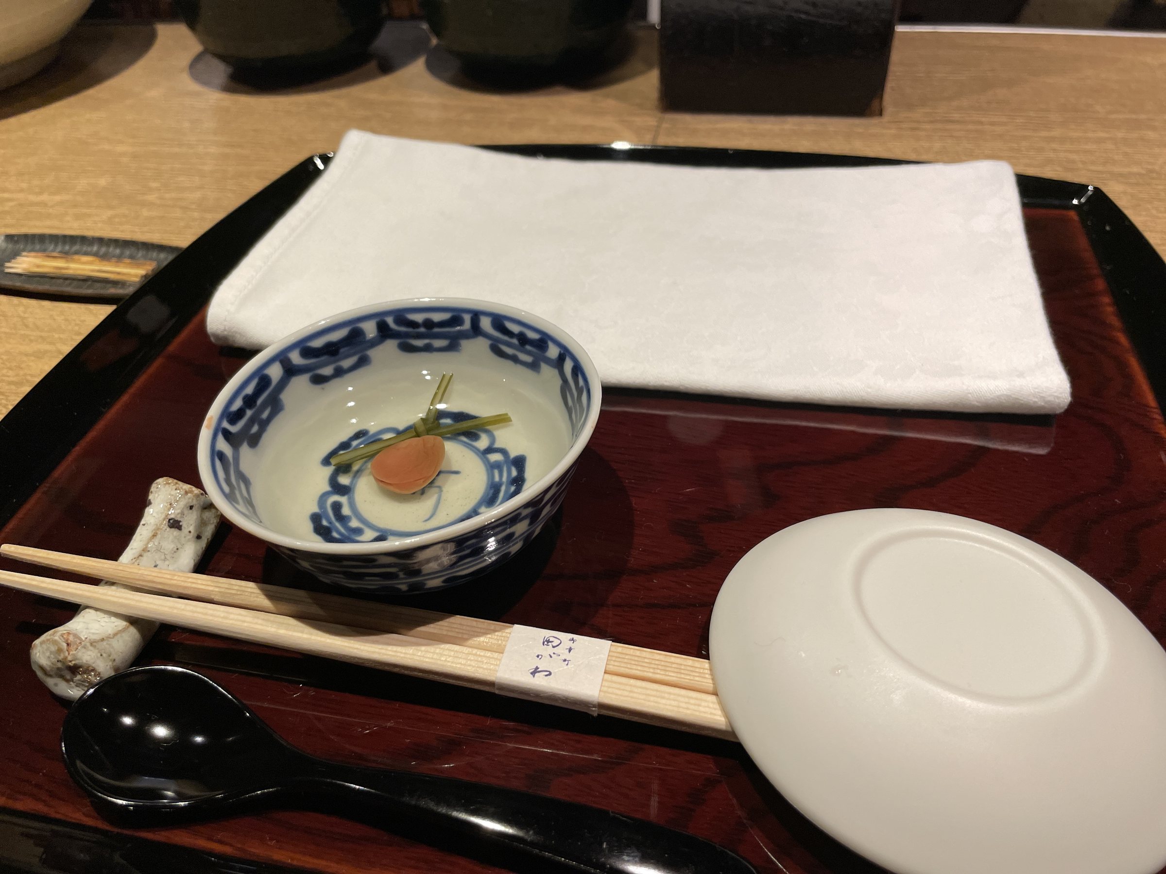 A place setting with the welcome cup of hot water, a pickled plum at its center.