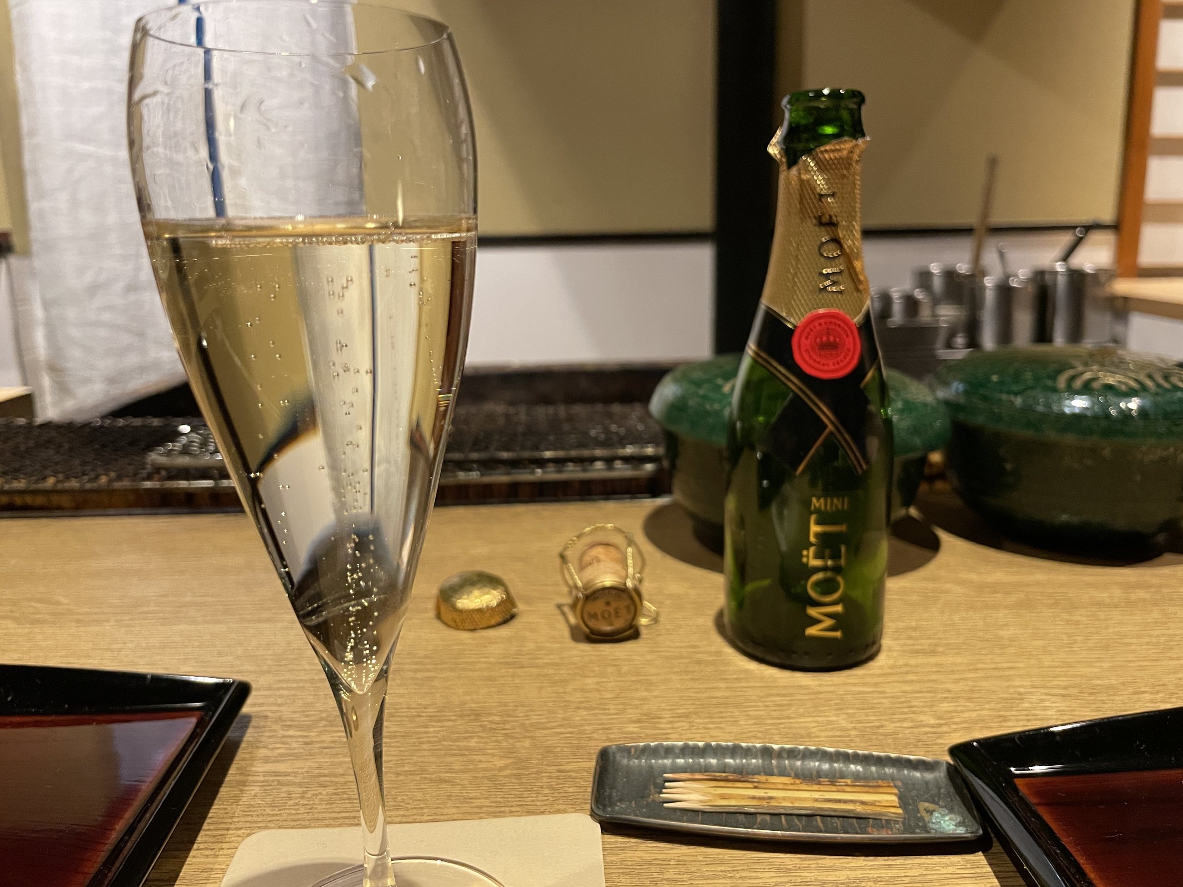 A flute of champagne beside a miniature bottle.