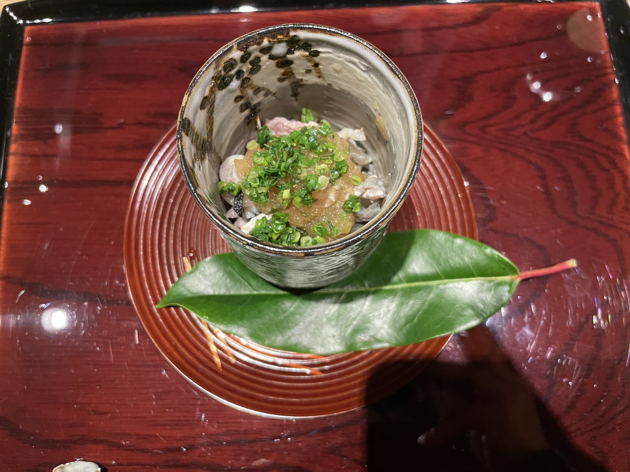 A glass of fugu skin dressed with ponzu and spring onion, set on a leaf.