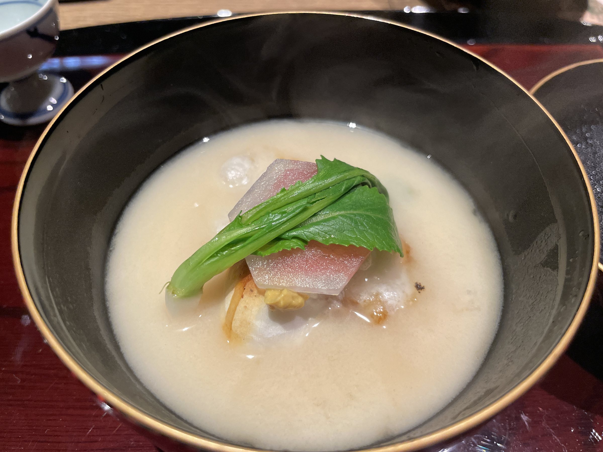 White miso zoni with toasted mochi, a slice of vegetable and a green leaf.