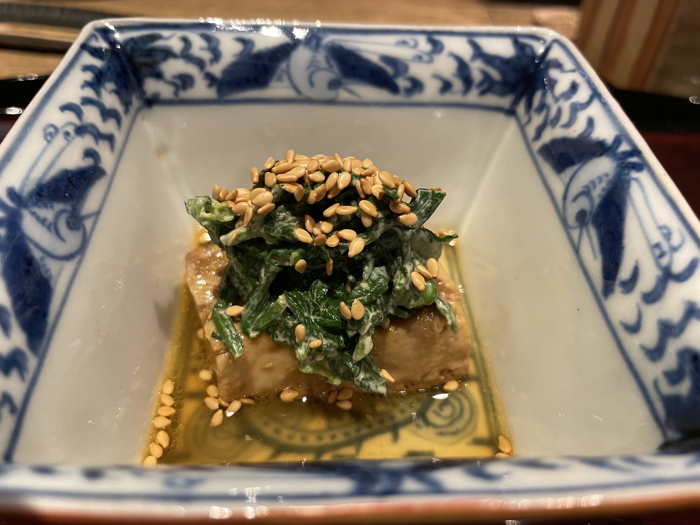 Monkfish liver under chopped chrysanthemum greens in a blue and white dish.