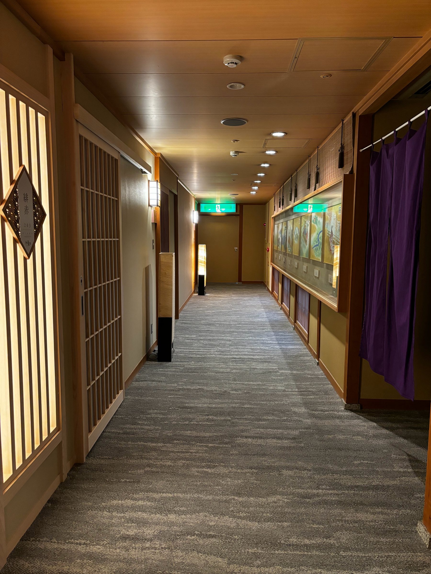 A carpeted corridor lined with lattice-fronted room entrances, softly lit.