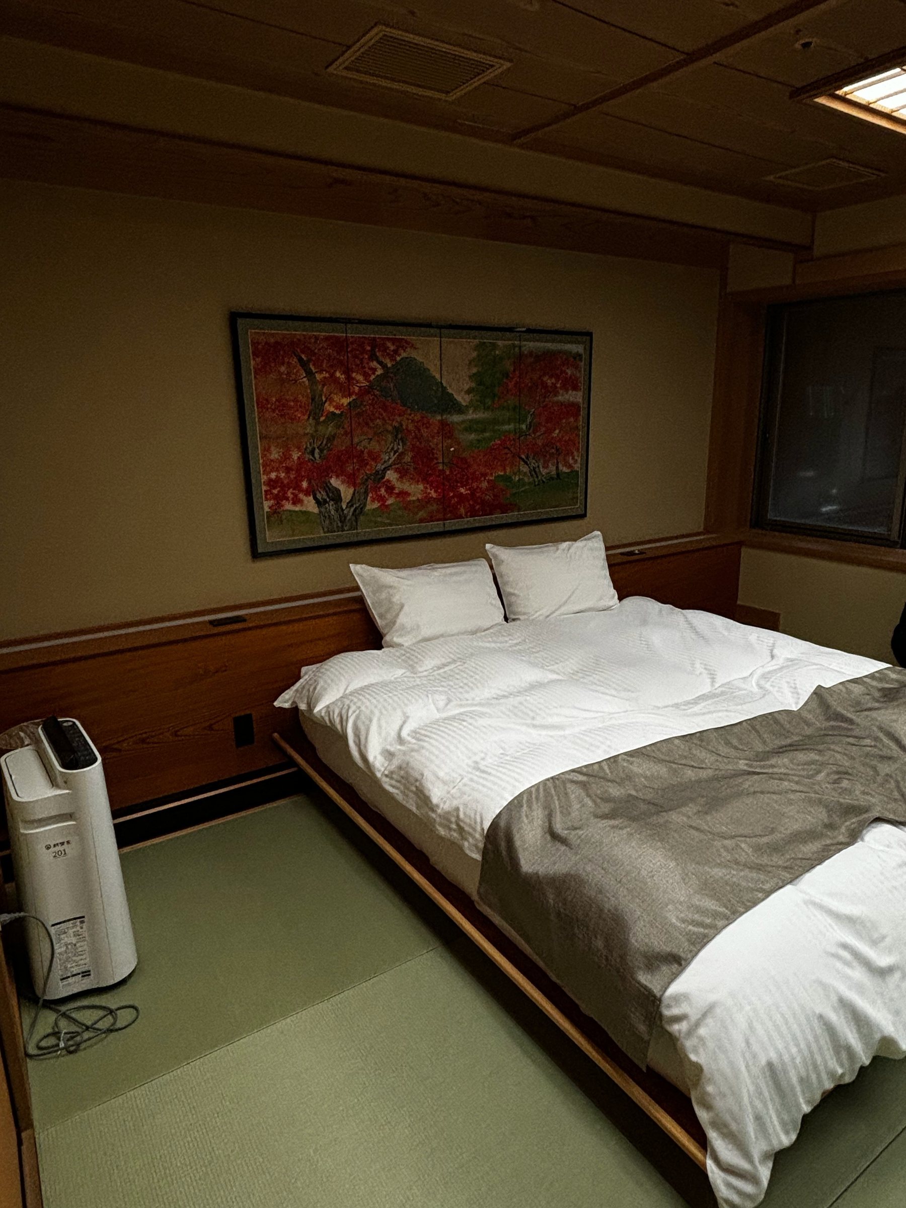 Twin beds set against a large painting of autumn maples.