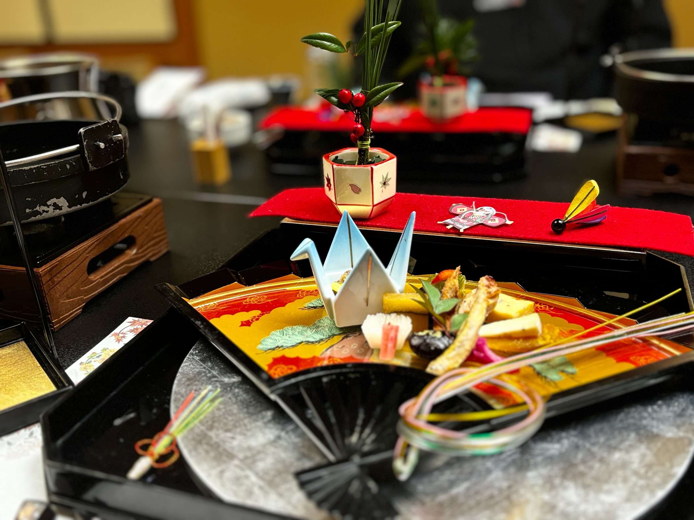 The first tray of dinner: a fan-shaped platter with a folded paper crane and a small pine arrangement.