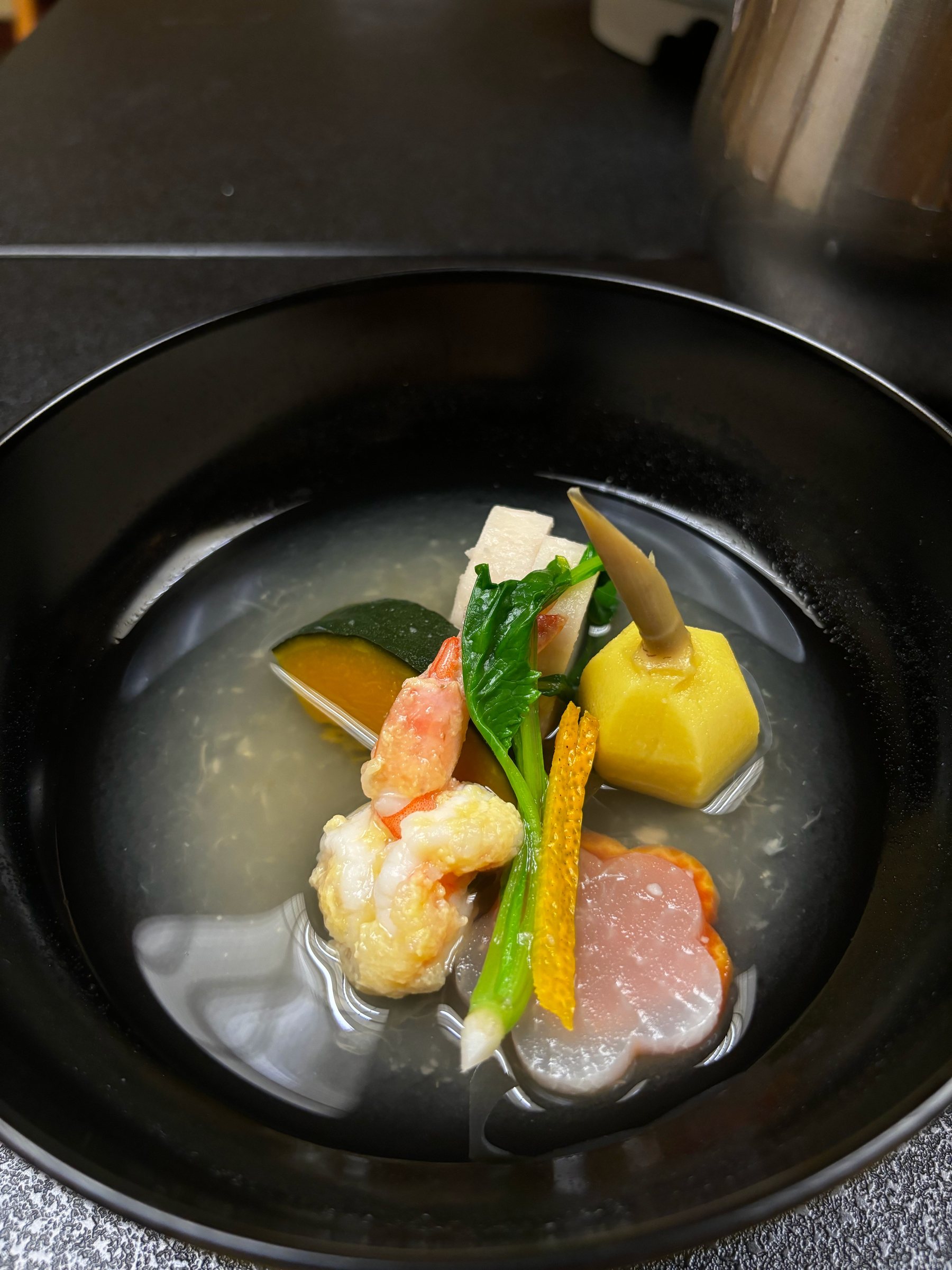 A clear soup with prawn, kabocha and arrowhead in a black lacquer bowl.