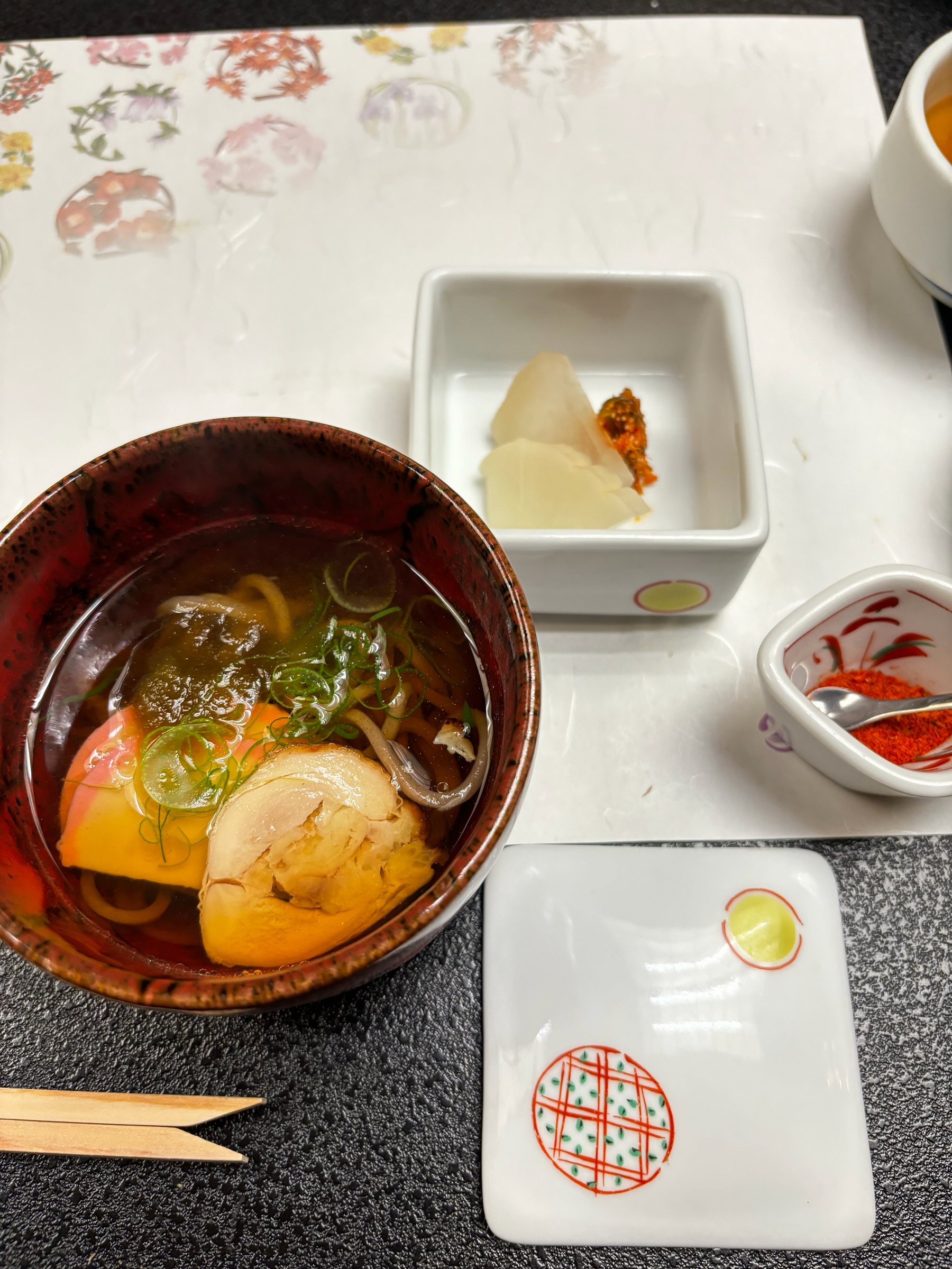 Warm soba with chicken, kamaboko and green onion, beside pickles.