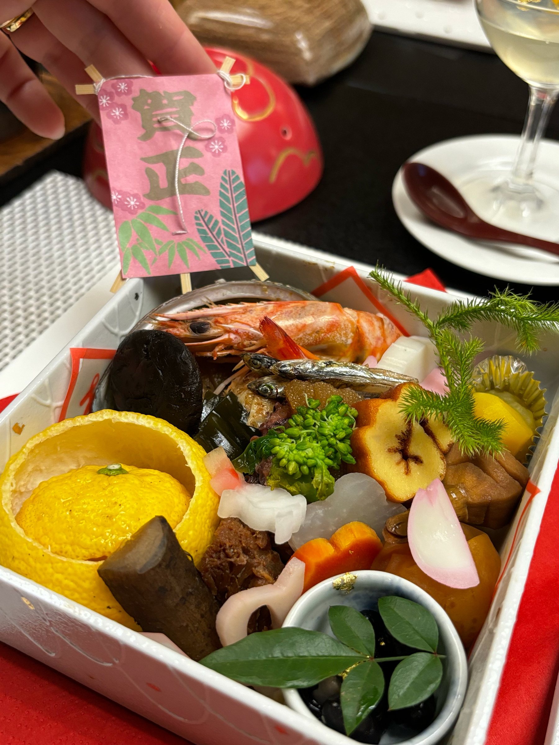 The tiered box of New Year dishes, with prawns, a yuzu cup and black beans.