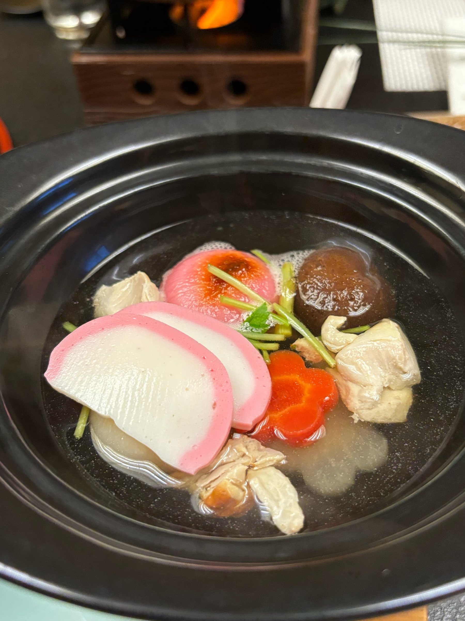 Ozōni in a black lacquer pot: red and white kamaboko, mochi, a carrot flower and shiitake.